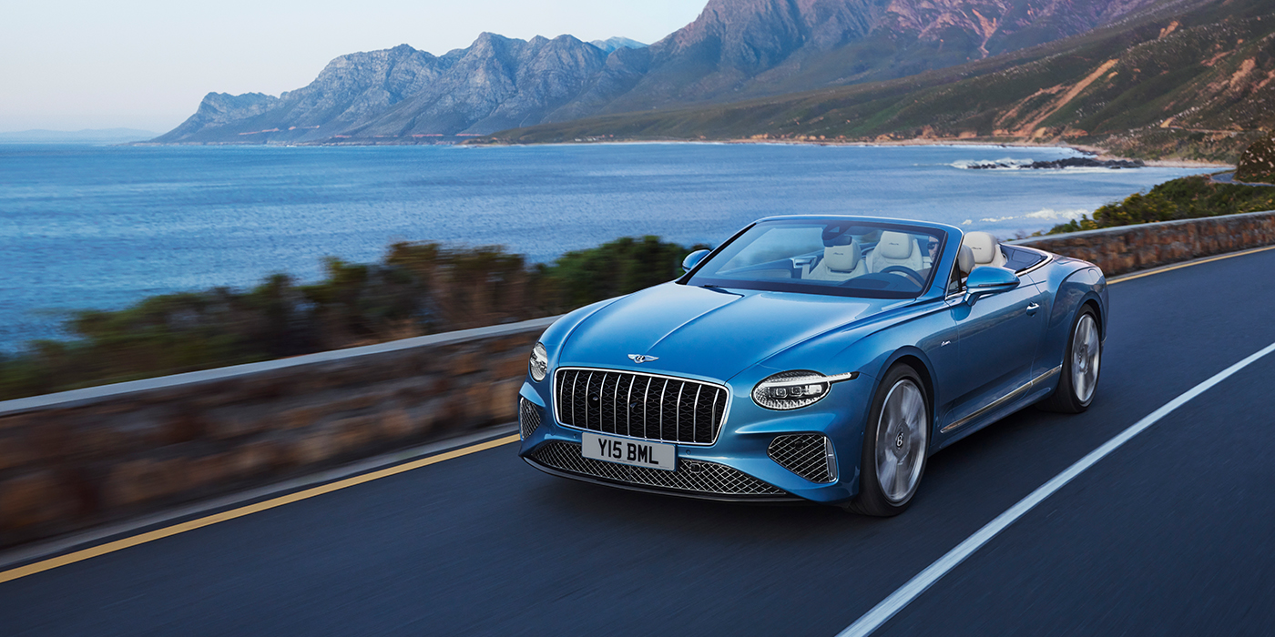 Bentley Oslo New Bentley Continental GTC Azure convertible in Light Windsor blue paint with 22 inch Azure wheels and chrome grill, driving dynamically by the sea