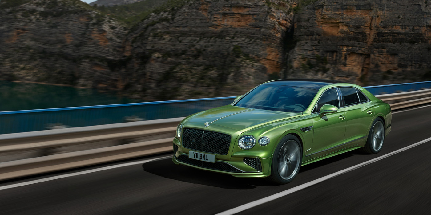 Bentley Oslo Bentley New Flying Spur Speed v8 hybrid sedan driving dynamically on a mountain road in Tourmaline Green paint