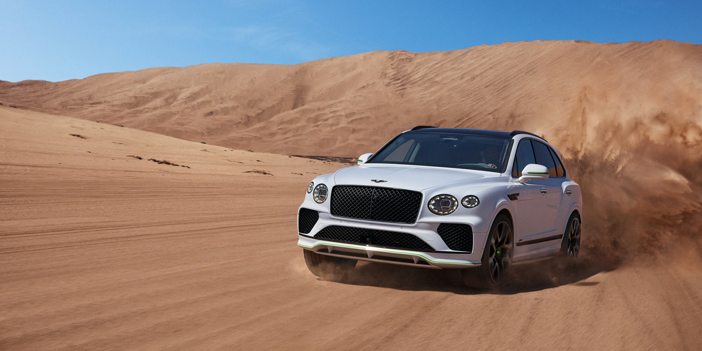 Bentley Oslo Bentley Bentayga Speed SUV front three quarter in Snow Quarts Pearlescent by Mulliner white paint driving dynamically through the desert