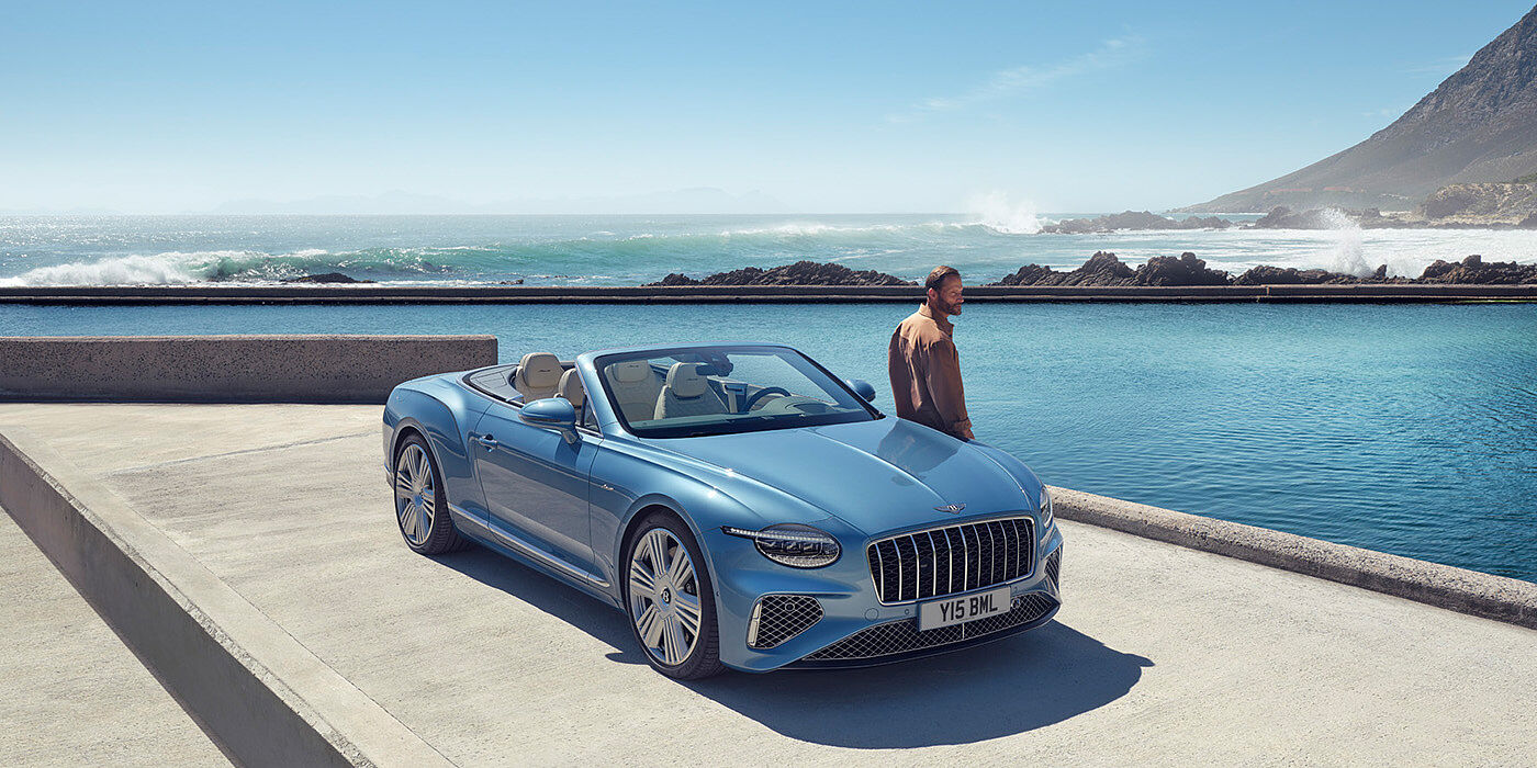 Bentley Oslo New Bentley Continental GTC Azure convertible front view in Light Windsor blue paint with 22 inch ten spoke wheels parked by the sea in the sunshine