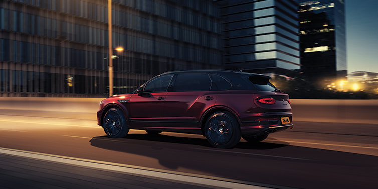 Bentley Oslo Bentley Bentayga Extended Wheelbase Mulliner SUV in Cricket Ball red paint driving dynamically in city at night